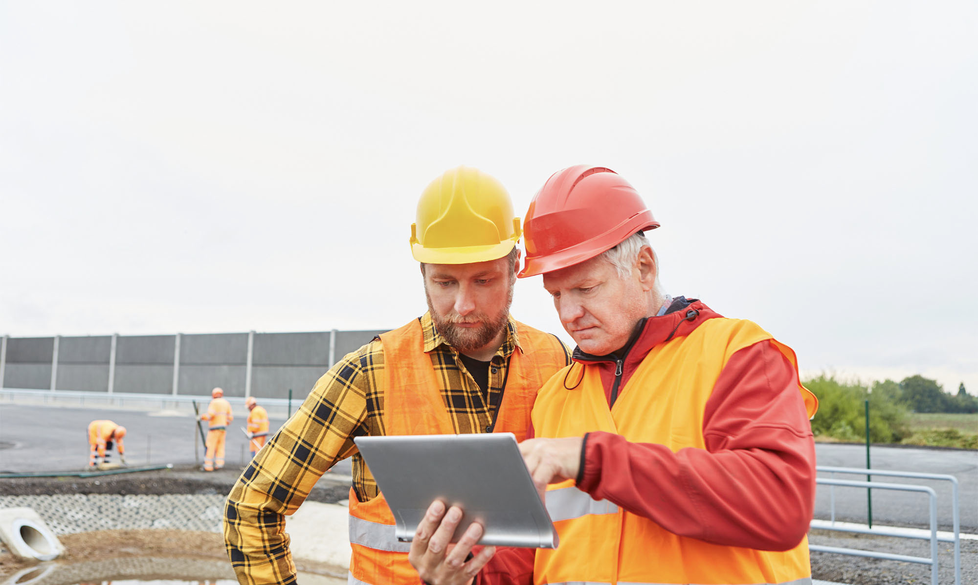 Construction workers in conversation, looking at tablet computer.