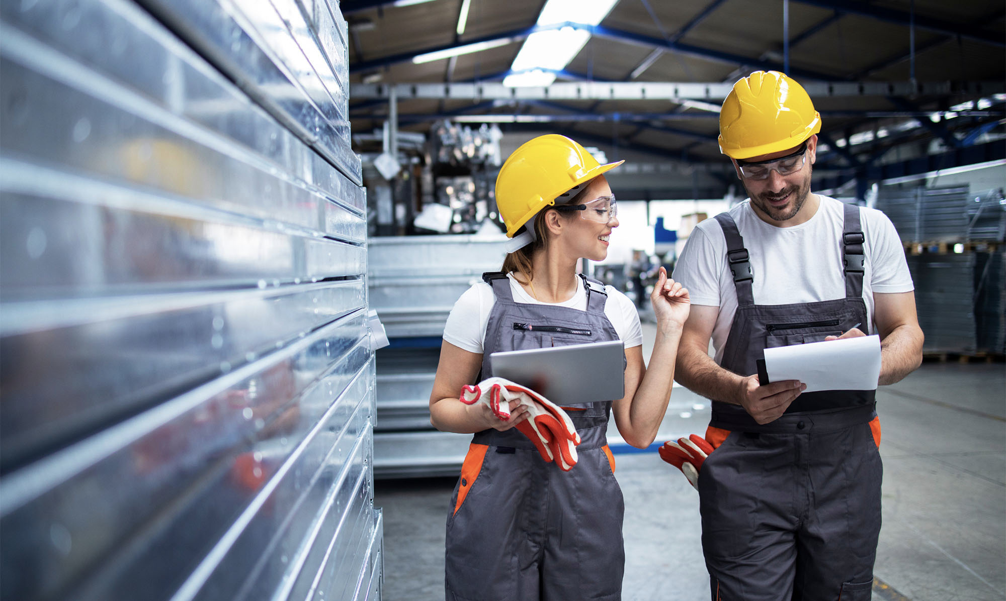 Two factory workers wearing safety gear in conversation.